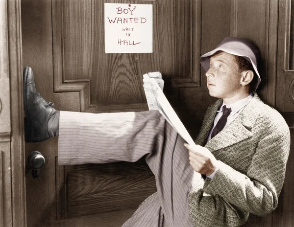 Man leunend tegen een deur met zijn benen omhoog en lezen van een krant — Stockfoto