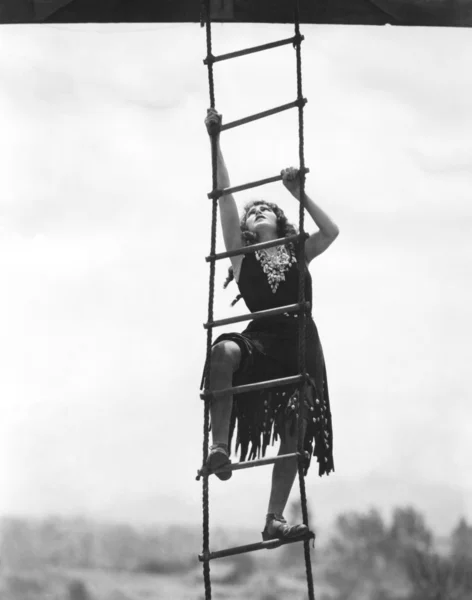 Woman climbing up a rope ladder Stock Photo