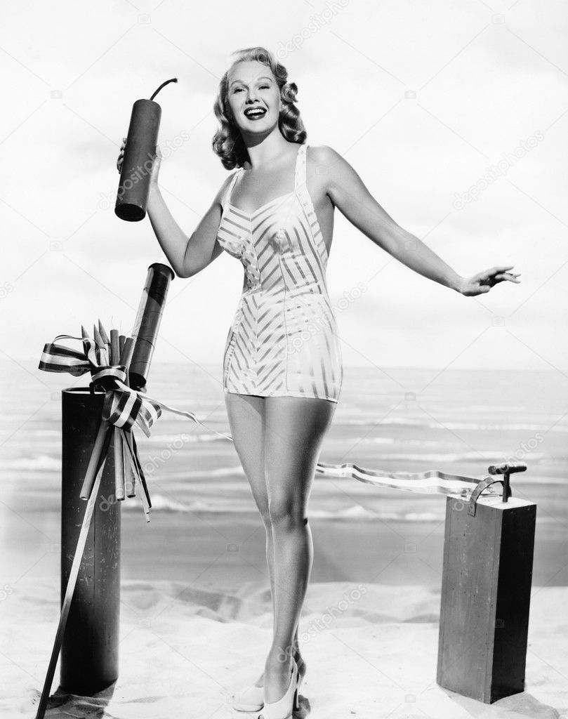 Woman in a bathing suit at the beach holding an oversized fire cracker in her hands