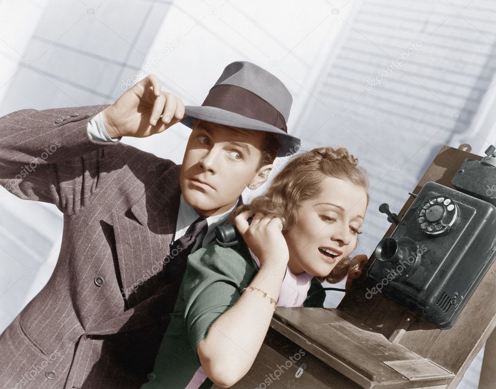 Man and woman listening on an outside telephone
