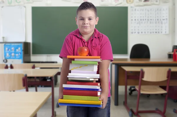 Мальчик с стопкой книг в классе — стоковое фото