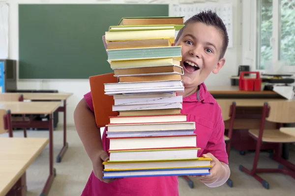 Gelukkige jongen met stapel boeken in een klaslokaal — Stockfoto