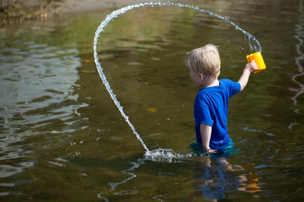 stock image Boy tosses water from cup in lake