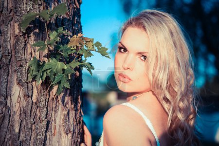 Jeune femme blonde à côté d'un arbre 